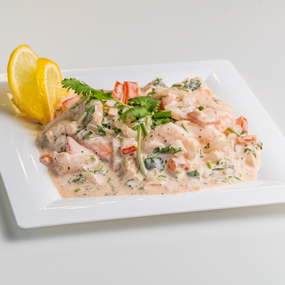 Creamy seafood ceviche with shrimp, red peppers, and cilantro, garnished with lemon wedges.
