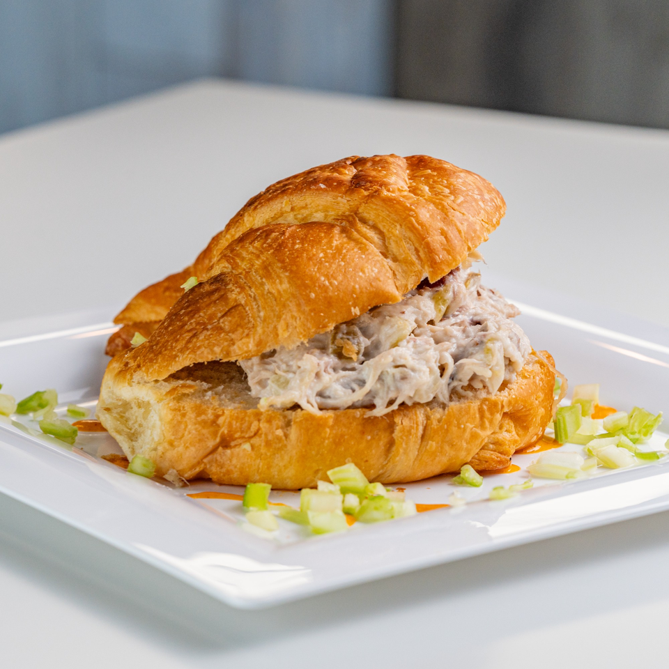 A crab salad croissant sandwich on a white plate, garnished with chopped celery.